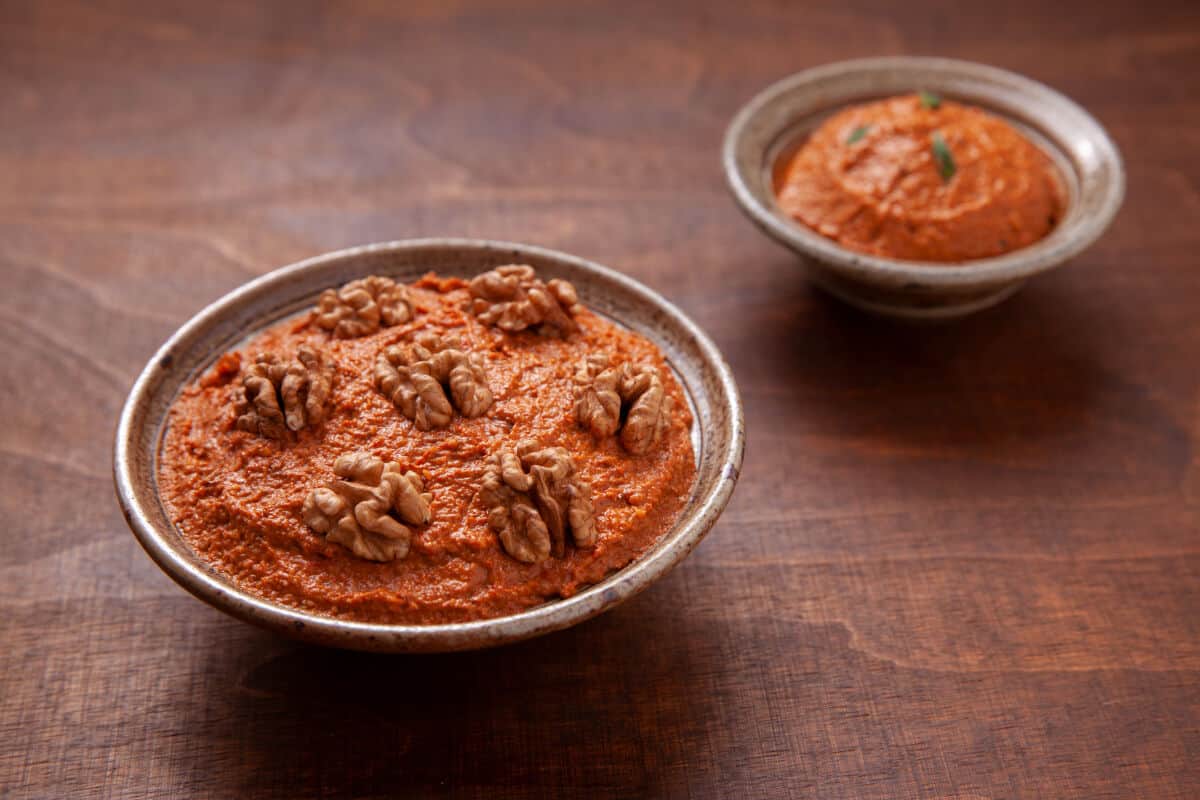 A large bowl of acuka in the foreground with 7 whole walnuts on top, with a smaller bowl of acuka in the backgro.