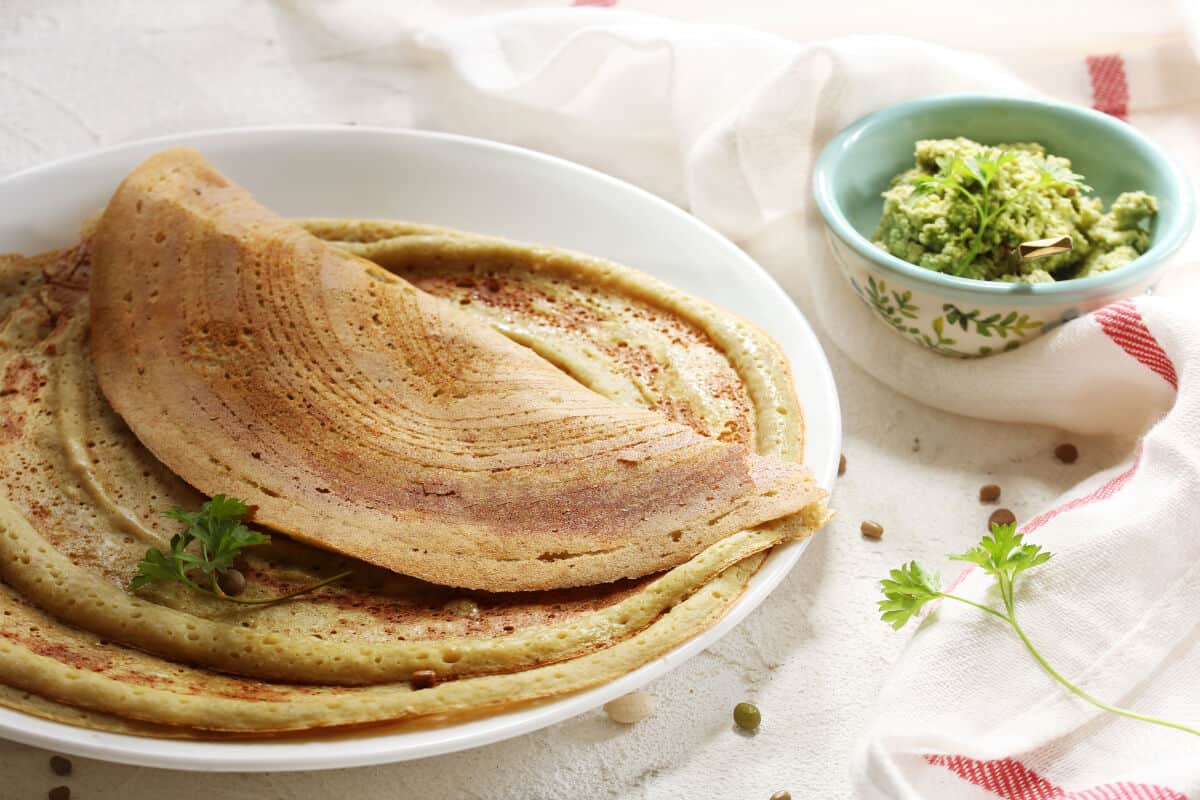 A large plate with a handful of adai on, next to what looks like a bowl full of guacamole in the backgro.