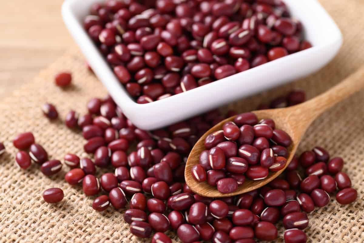 A white bowl and wooden spoon full of adzuki beans, all sitting on a hessian table cl.