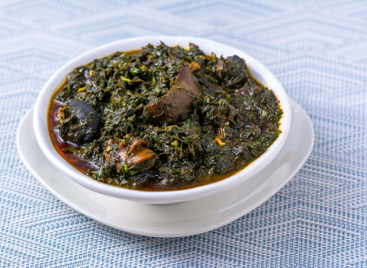A close up of a bowl full of afang soup, on a small white plate on a blue tablecl.