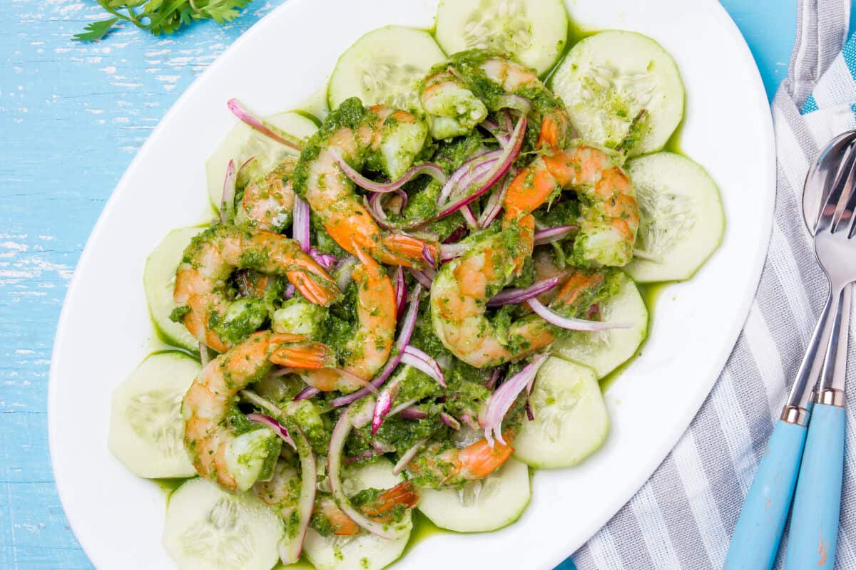 An oval platter covered with cucumber slices, and shrimp and blended chilis laid on .