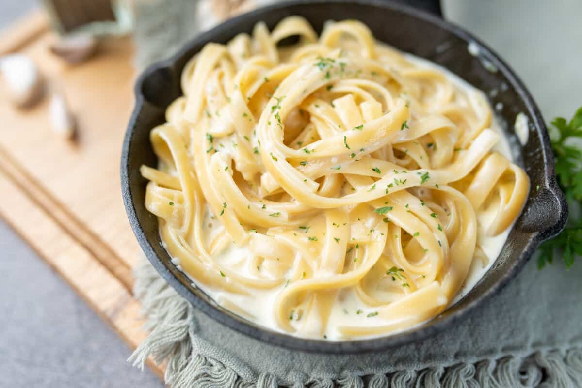 A black bowl full of ribbon like pasta coated in alfredo sa.