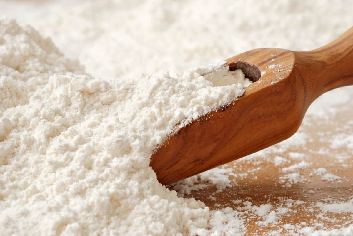 A pile of all-purpose flour, with a wooden scoop inserted in from the ri.