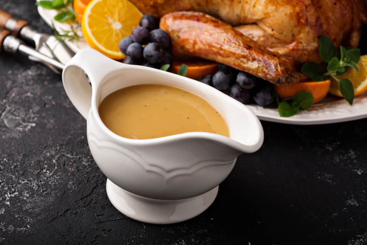 A white gravy boat full of allemande sauce, in front of a roast chicken din.