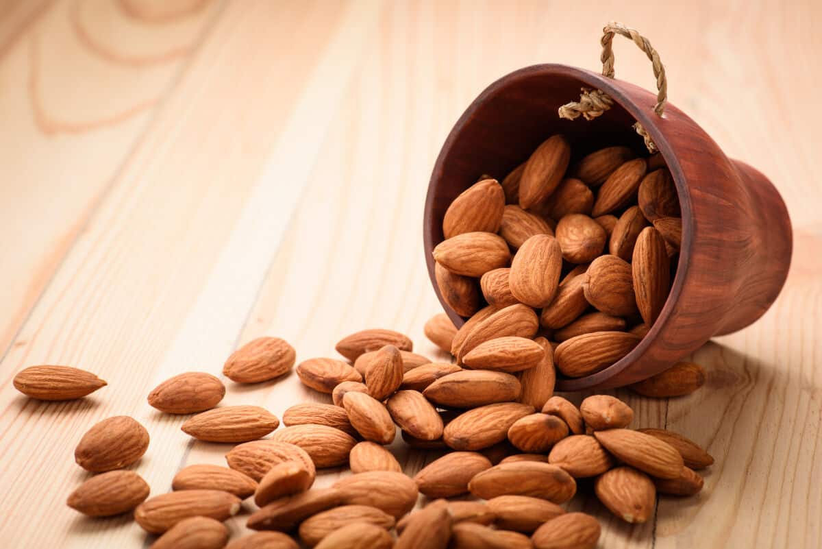 A small pot of almonds tipped over on to its side so that the almonds spill across a ta.