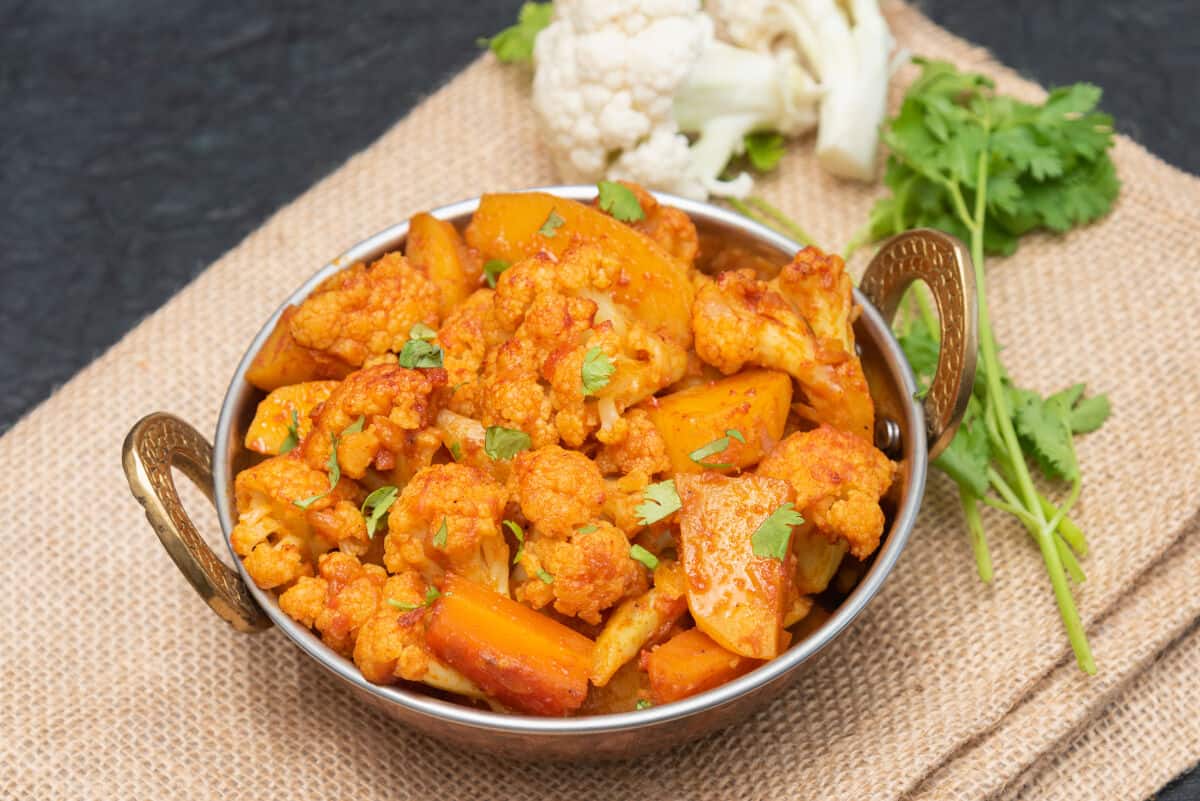 A small metal dish with two handles, full of curried cauliflower and potato, aloo g.