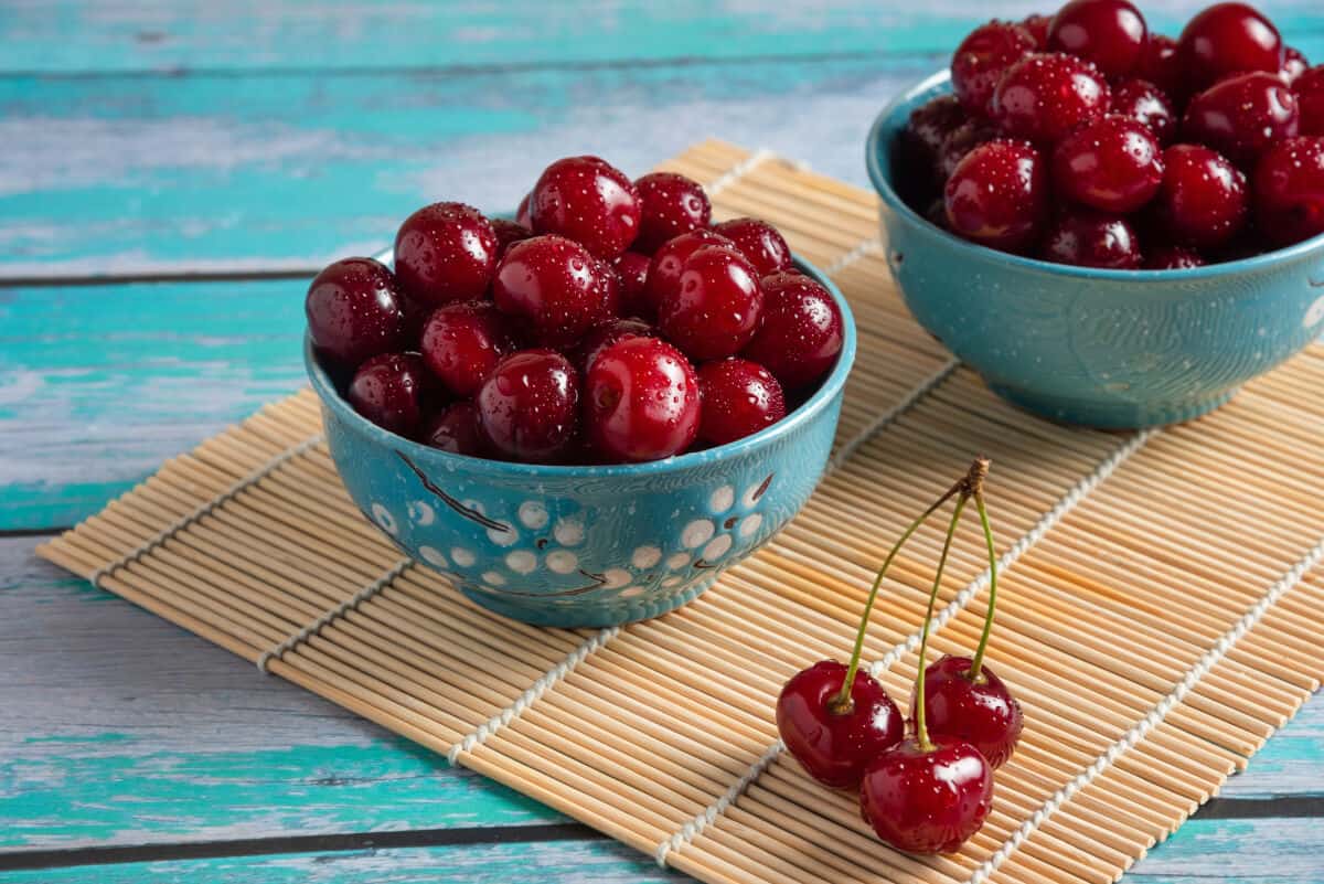 Two blue bowls full of amarelle cherries that are glistening with water dropl.