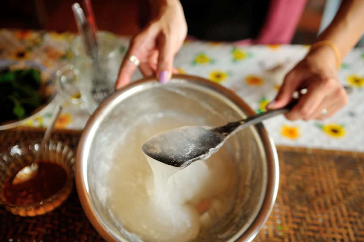 Sticky, gelatinous ambuyat dripping from a spoon back into a large b.