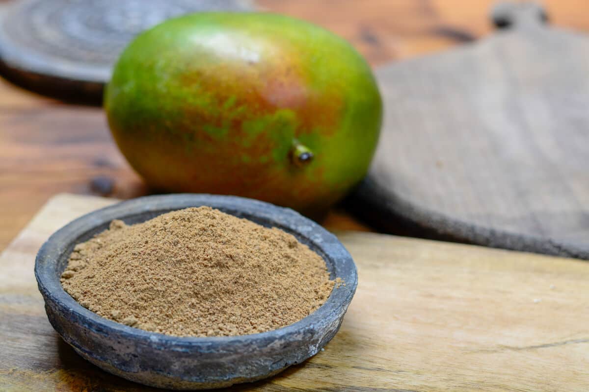 A small charcoal bowl full of amchoor, in front of a green unripe man.