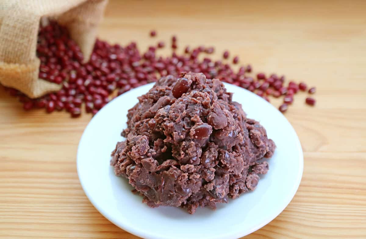 Anko paste on a small white plate, with a small sack of red beans spilling onto the table in the backgrou.