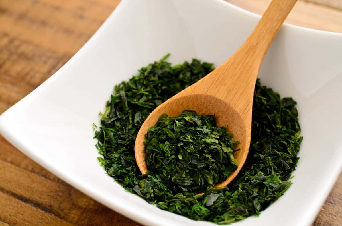 A small square dish half full of aonori, with a small wooden spoon ins.