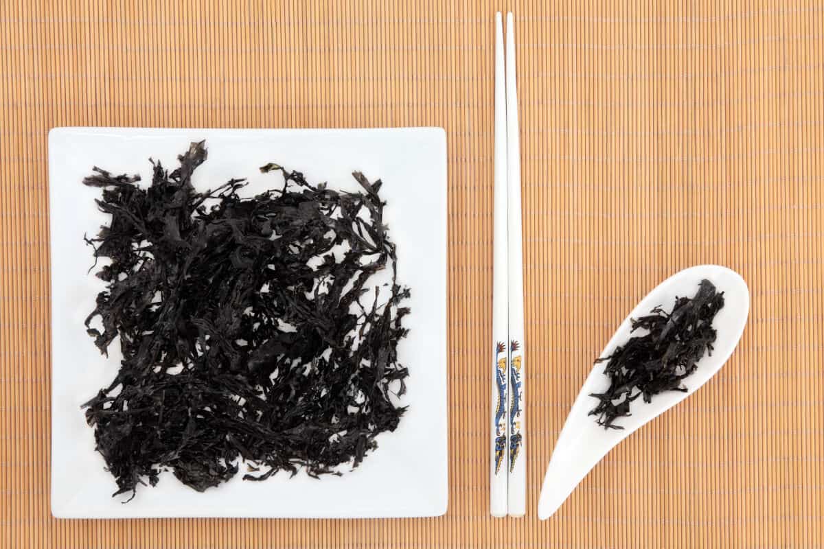 A plate  and spoon full of arame seaweed, with two chopsticks on the table in betw.