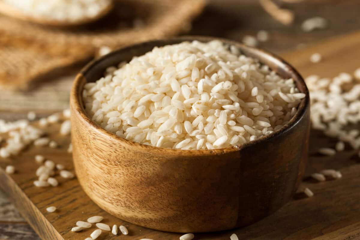 Close up of a brown wooden bowl of uncooked arborio r.