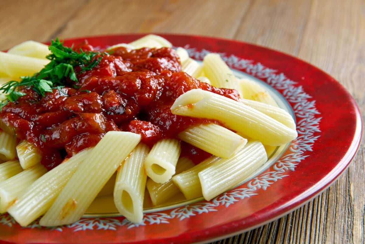 A close up of some penne pasta with a large helping of arrabbiata sauce on top and a sprig of pars.