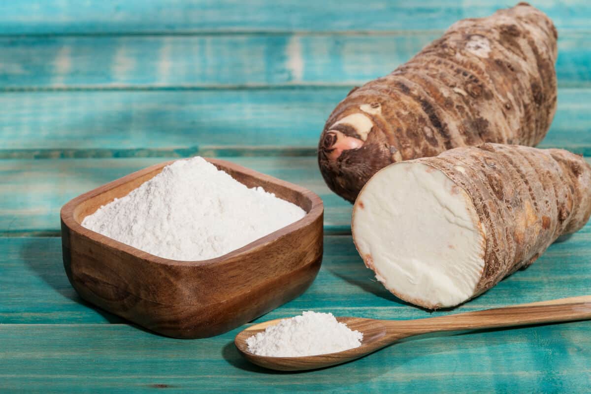 A bowl full of powdered arrowroot, next to a whole root and a half root showing the white ins.