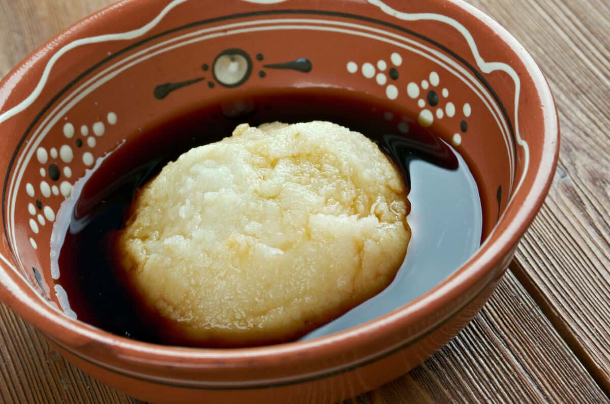 A small brown bowl of dark liquid, with some asida sitting in the mid.