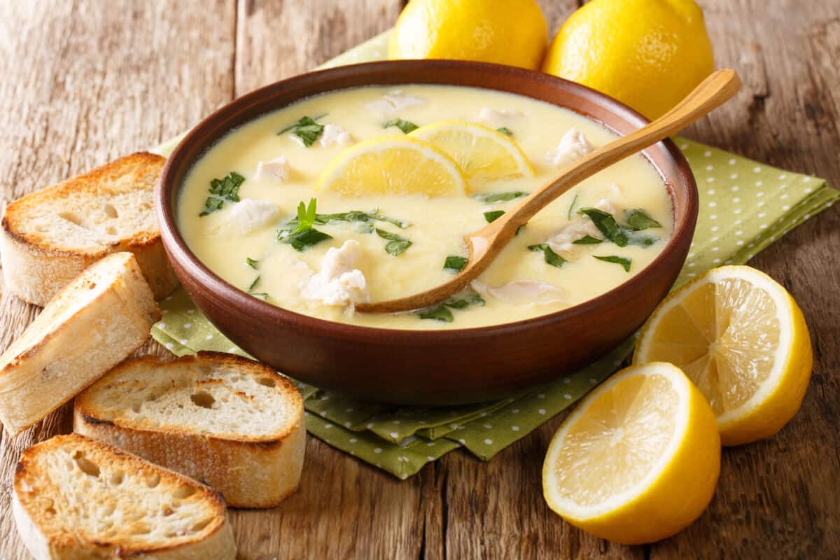A nice looking bowl of avgolemono soup, surrounded by lightly toasted bread pieces and some lem.
