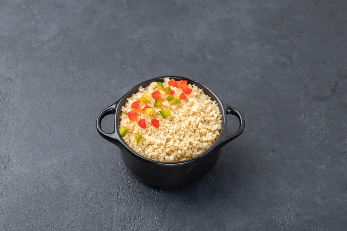 A small black bowl full of acheke, with that looks like small diced cucumber and tomato on .