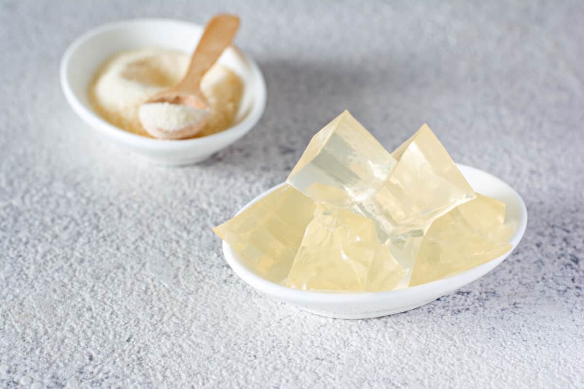 A white bowl full of agar cubes, next to a smaller bowl of agar pow.