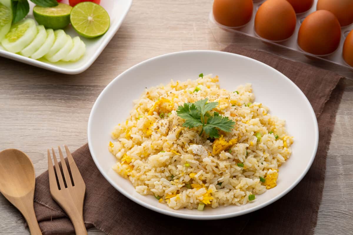 A white bowl full of arroz con huevos, on a brown napkin, next to a wooden fork and spo.