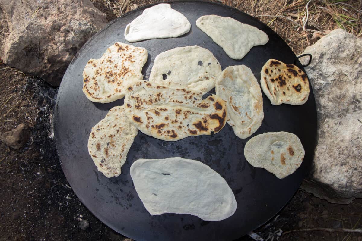 Ash cakes being made on the reverse of a large metal dish, over a fire contained by large sto.