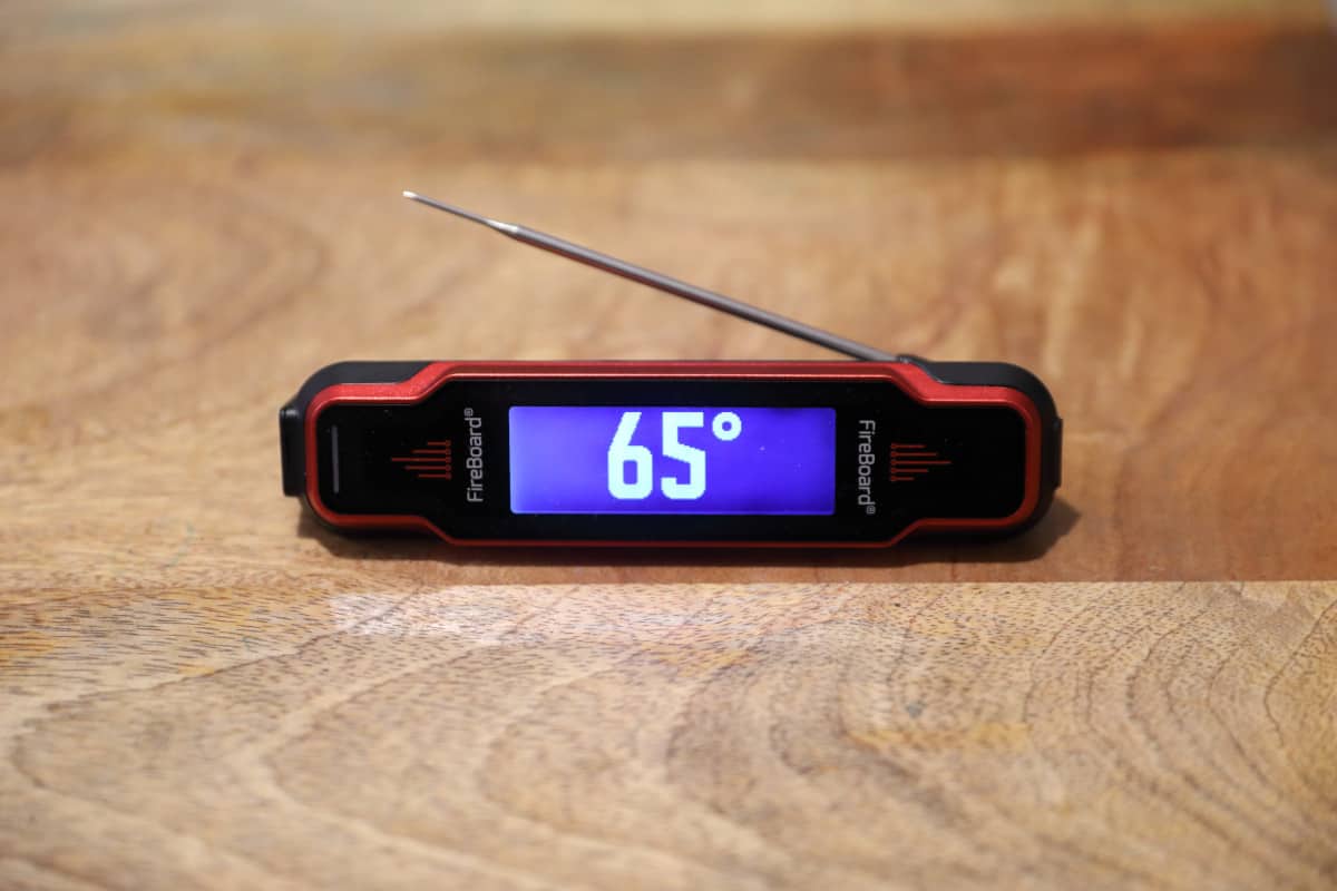 Fireboard Spark thermometer on a wooden cutting board showing 65 degrees F.