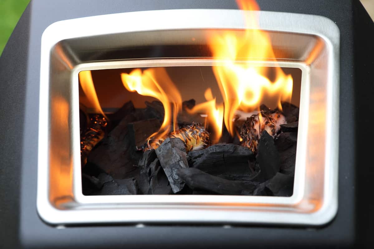 Looking inside the fuel hatch of the Ooni Karu 16, showing a charcoal fire being lit.