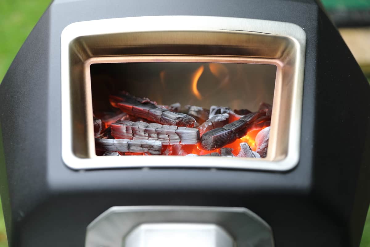 Looking inside the fuel hatch of the Ooni Karu 16, showing a wood fire with a low flame.