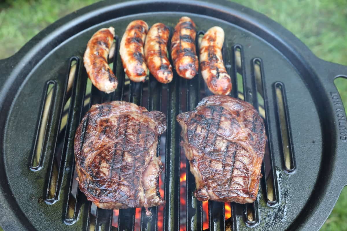 Five sausages and two steaks grilling on a Solo Stove Bonfire.