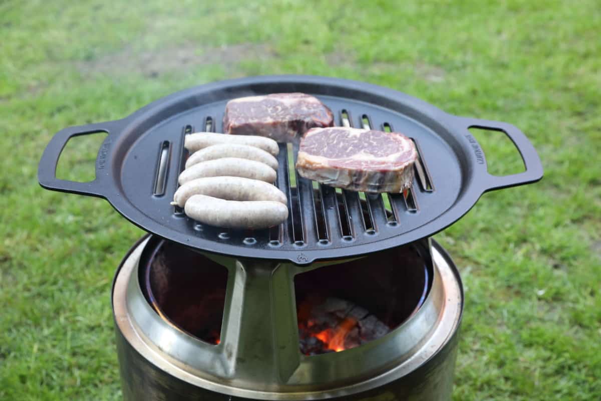 Sausages and steaks being grilled over a Solo Stove Bonfire.