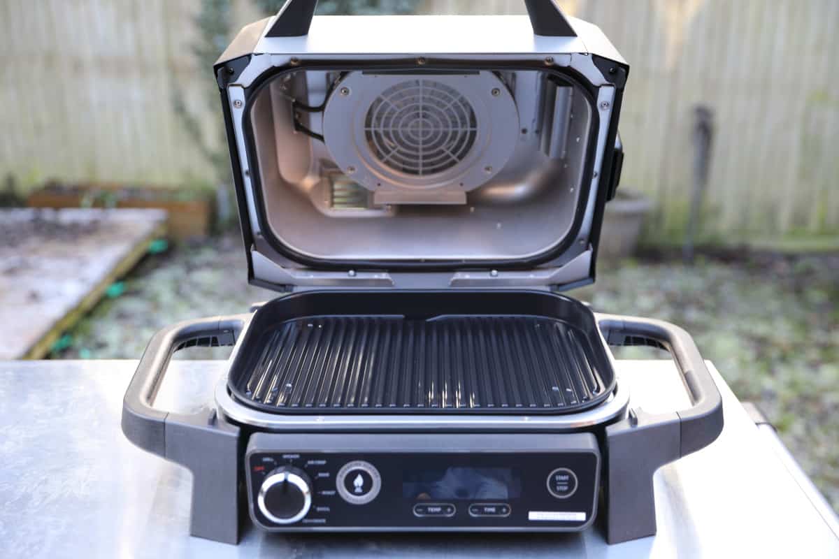 Ninja Woodfire on metal table with the lid open and the cast iron grate installed.