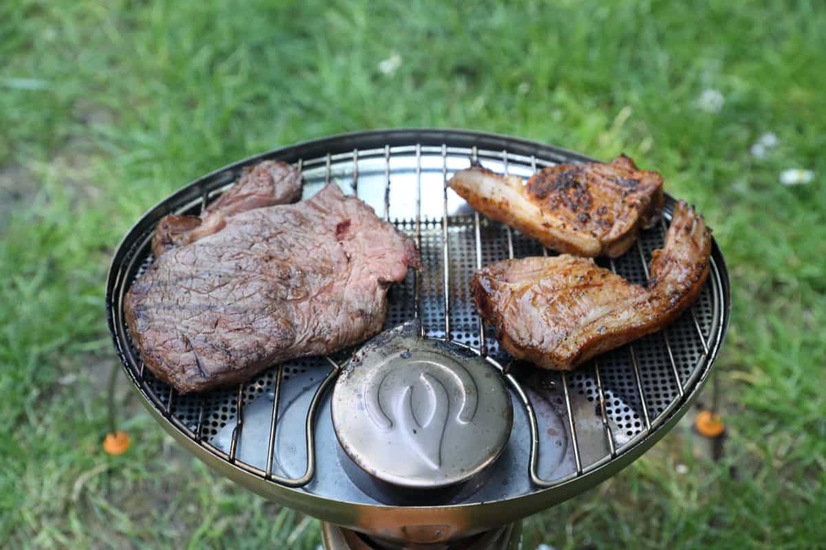 Two lamb chops and a steak being grilled on the Biolite CampStove.