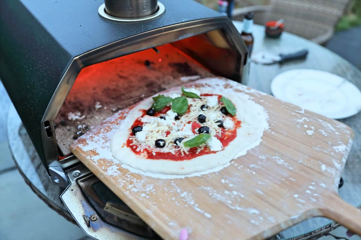 A medium siz3d pizza being slid into an Ooni Karu 16 from a bamboo pizza peel.