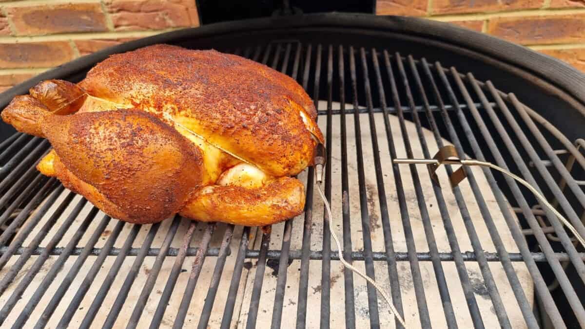 A whole smoked chicken on the grates of a kamado big joe smoker.