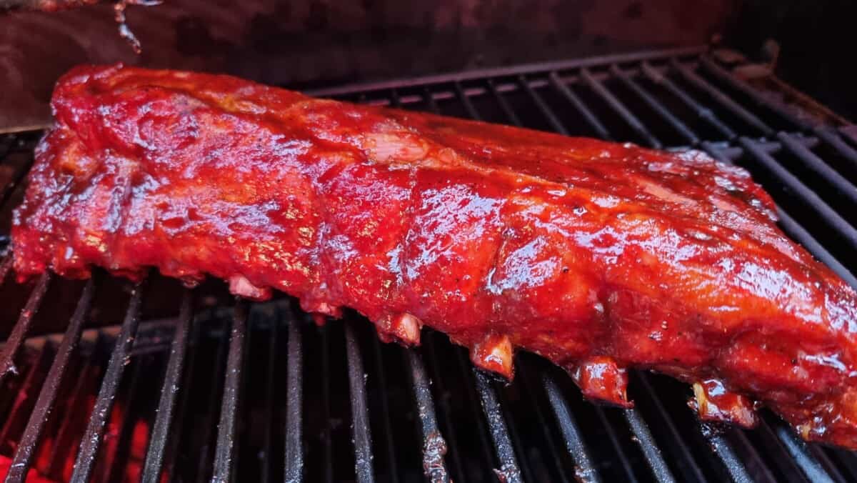 A sauce covered rack of baby back ribs on a smoker grate.