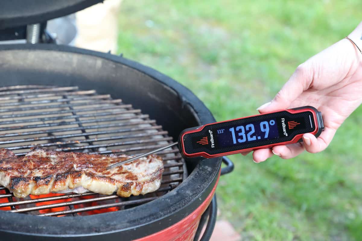 Fireboard Spark instant read thermometer in use, taking the temperature of a chicken on a red Kamado Joe Grill.