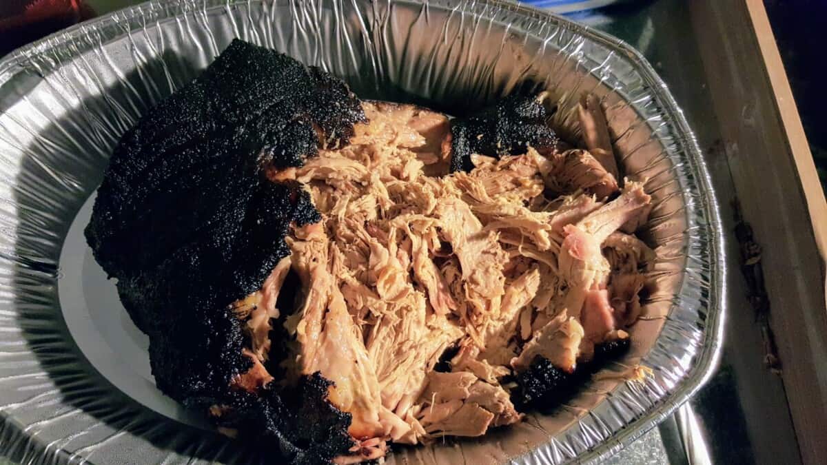 My pulled pork in a silver tray, partially pulled and with a deep black bbq bark.
