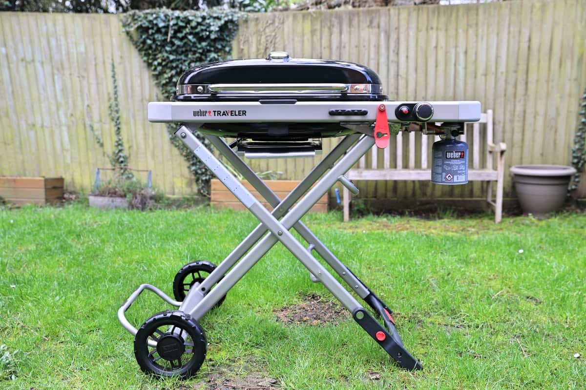 Weber Traveler gas grill, unfolded and standing on a grass lawn.