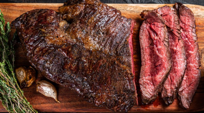 Grilled onglet steak, partially sliced, sitting on a cutting board.