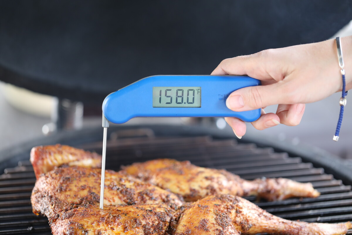 A blue instant read thermometer being used to measure the temperature of chicken.