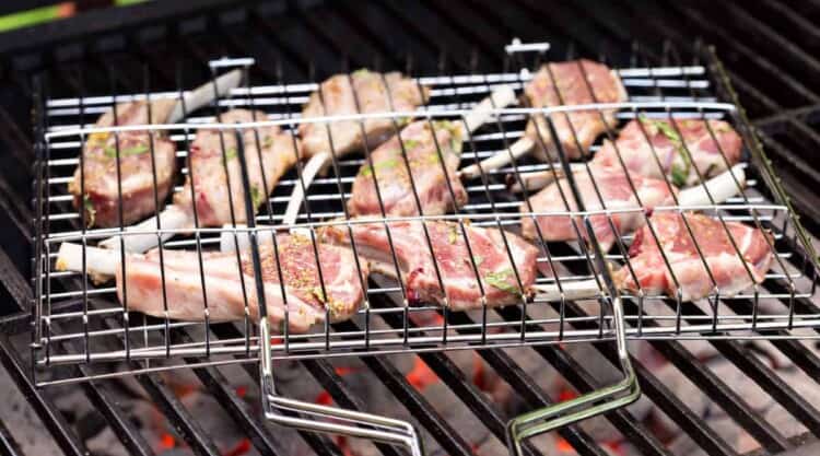 Close up of lamb cutlets in a grill basket over a charcoal grill