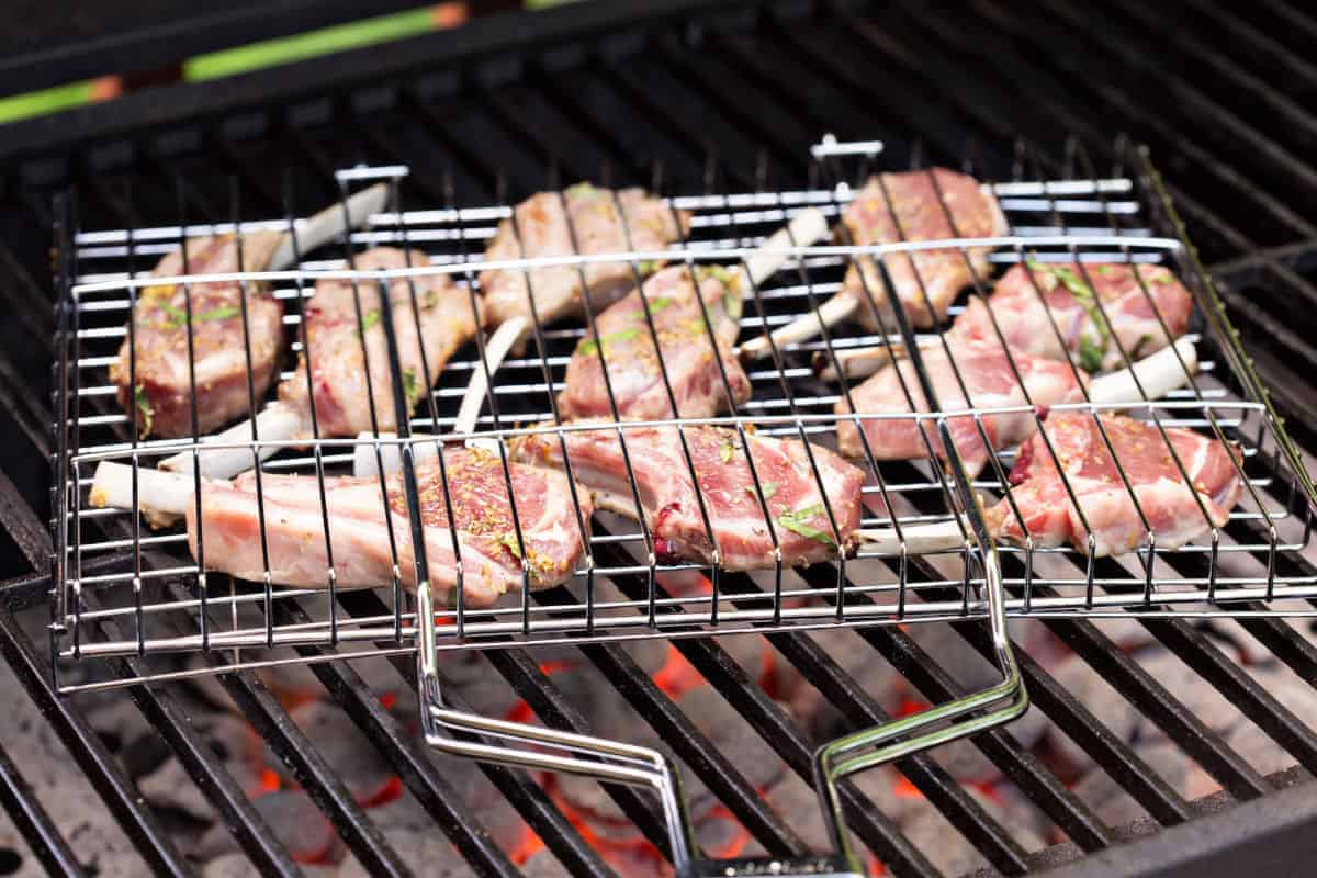 Close up of lamb cutlets in a grill basket over a charcoal grill