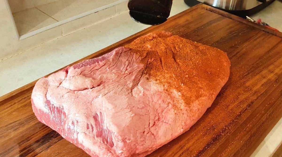A beef brisket being rubbed prior to grilling.