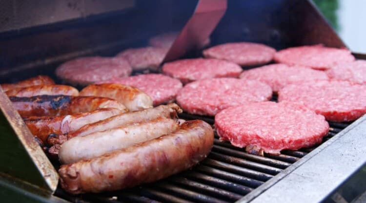 Burgers and sausages being grilled on a gas grill outdoors.