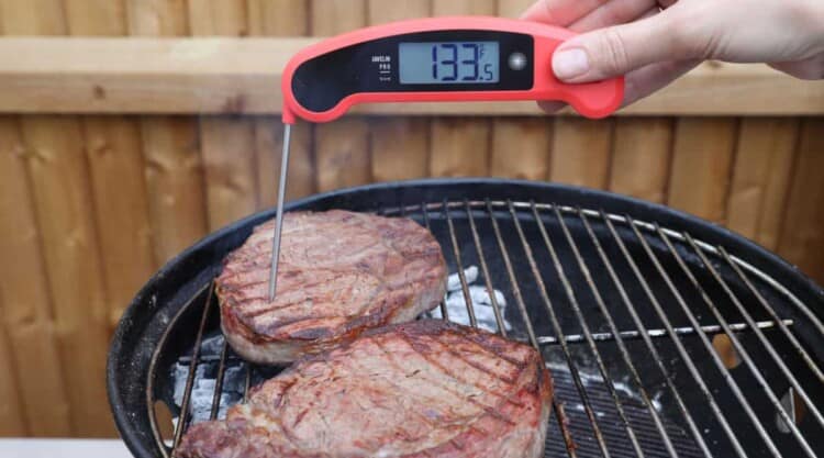 A red and black instant read thermometer reading 133.5 F in a steak