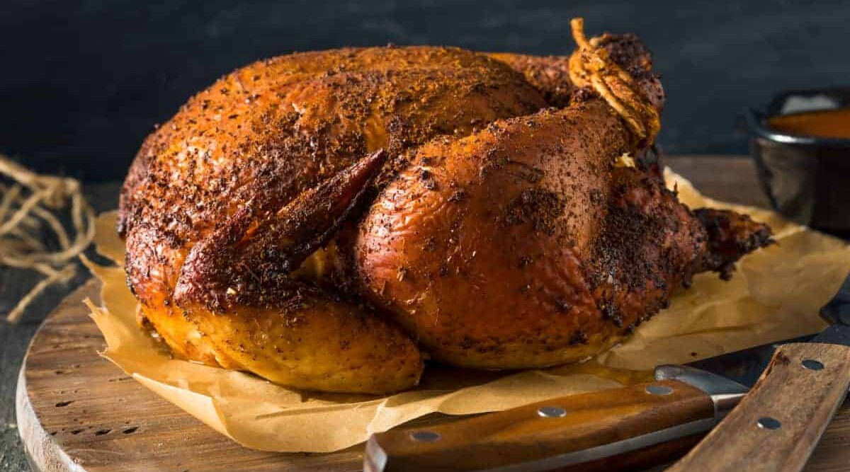 A smoked chicken with rub, on parchment paper on a chopping board ready for carving.