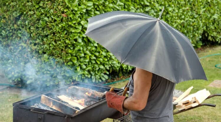 Man under an umbrella lighting a BBQ in the rain