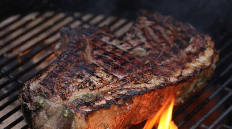 A bone in ribeye steak on a grill with flames licking around it